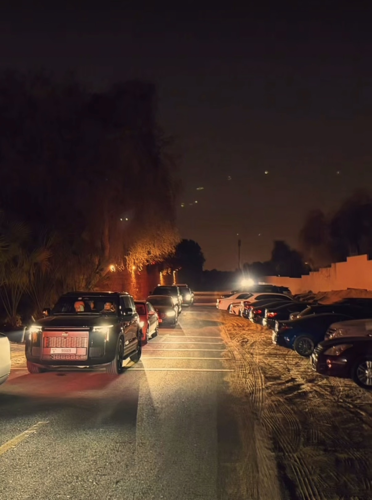 Vehicles arriving beside an organised parking area at night