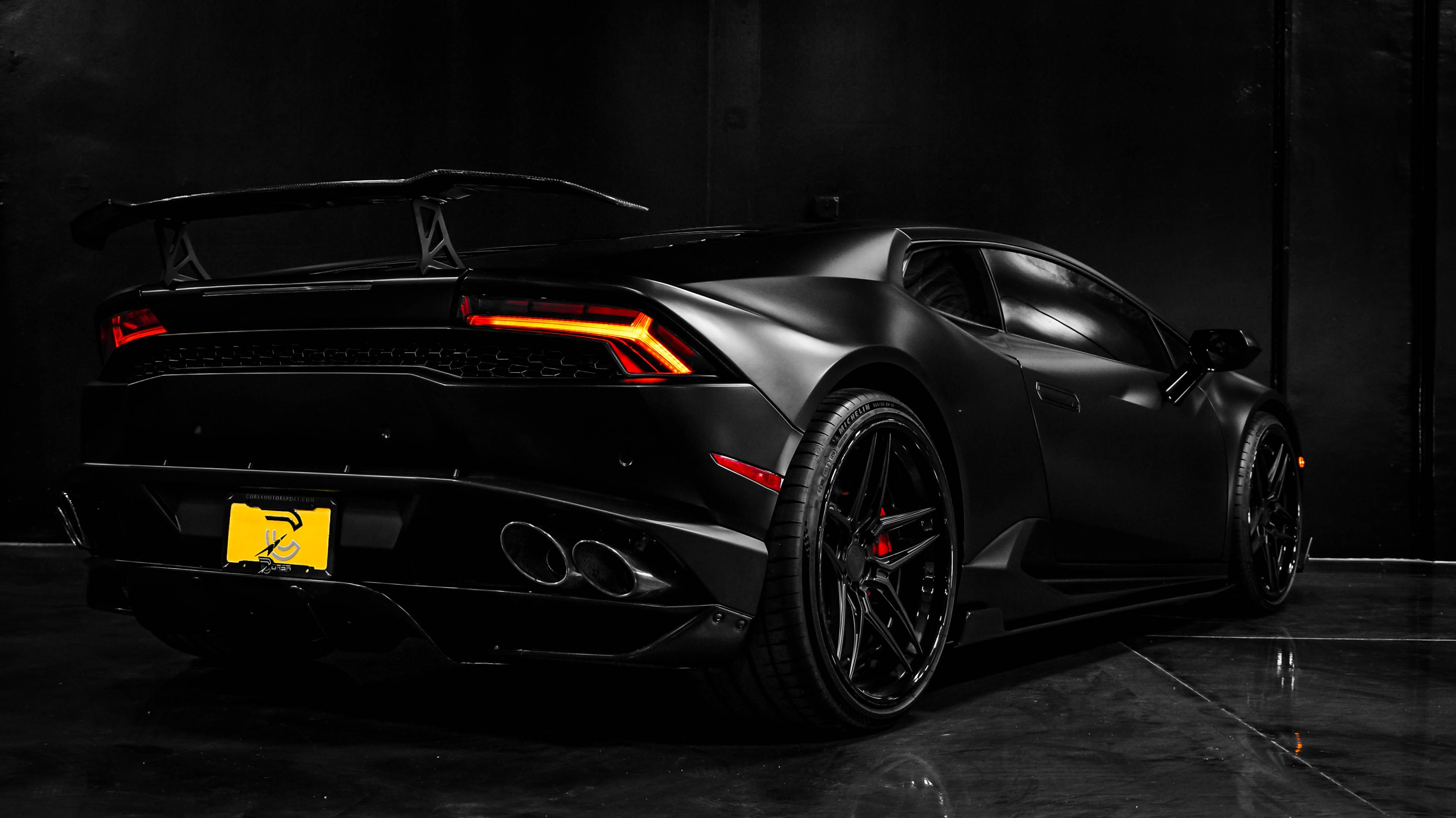 Rear three-quarter view of a matte-black Lamborghini in a dark showroom