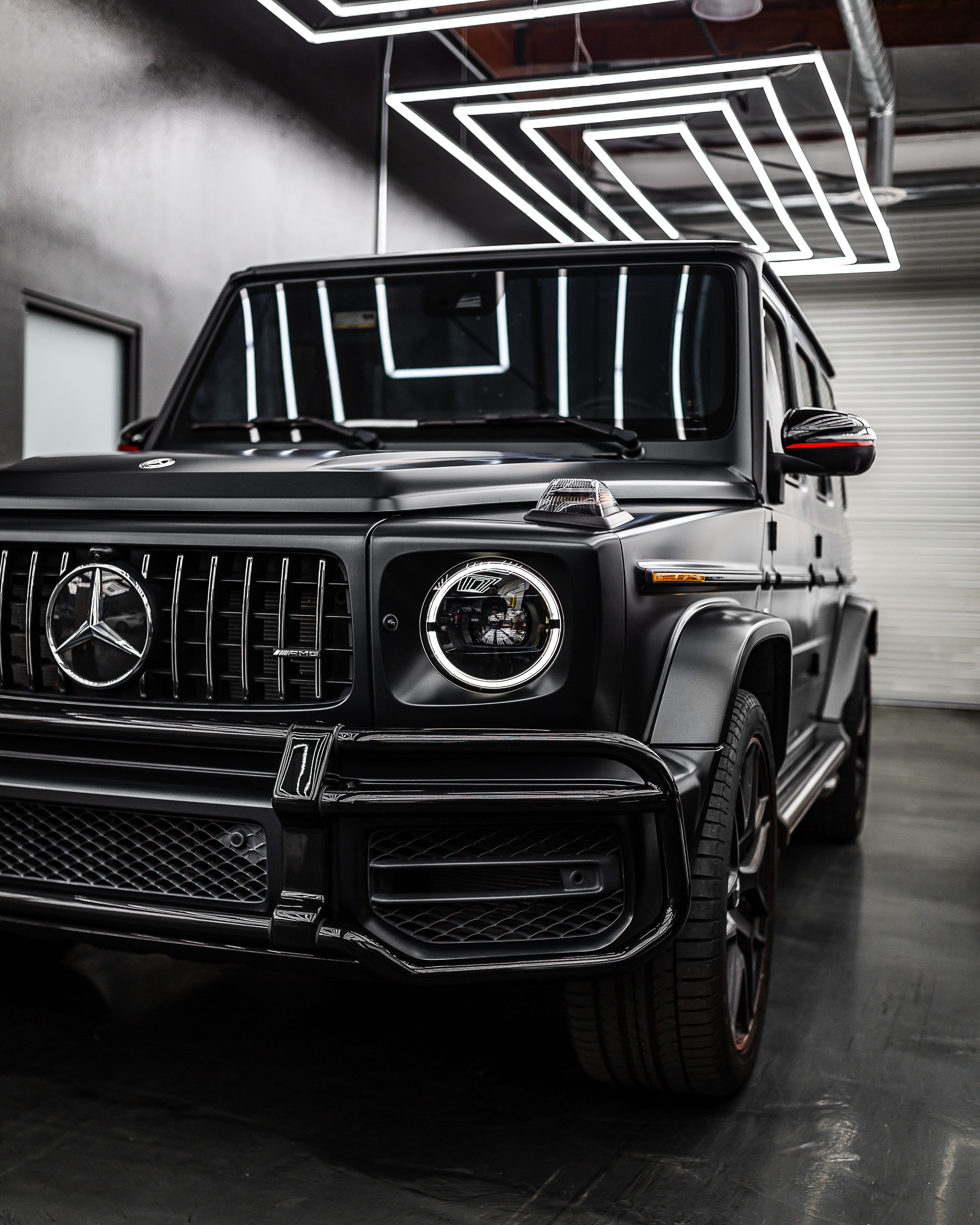 Front detail of a black Mercedes-Benz G-Class beneath geometric showroom lighting