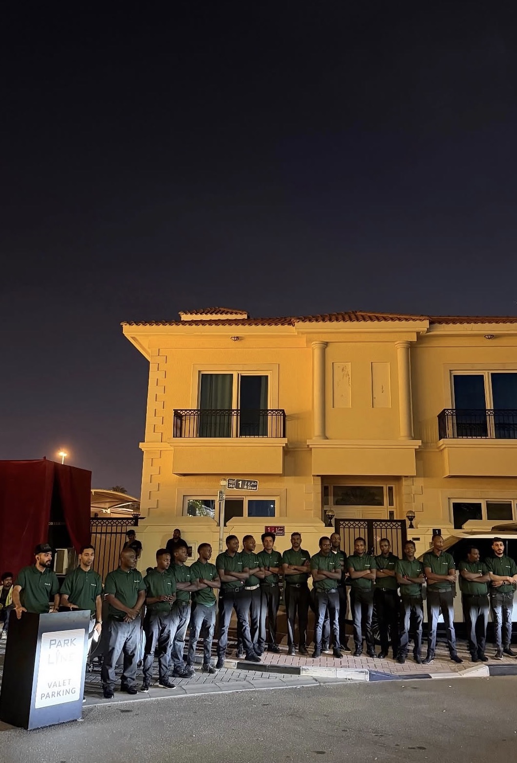 The Parkline valet team in green company uniforms standing beside the valet parking stand at night